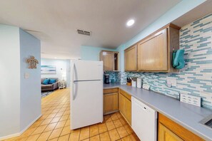 A kitchen with wooden cabinets, a white refrigerator, and a tiled backsplash. - Phoebe's Beach House (South Padre Island)