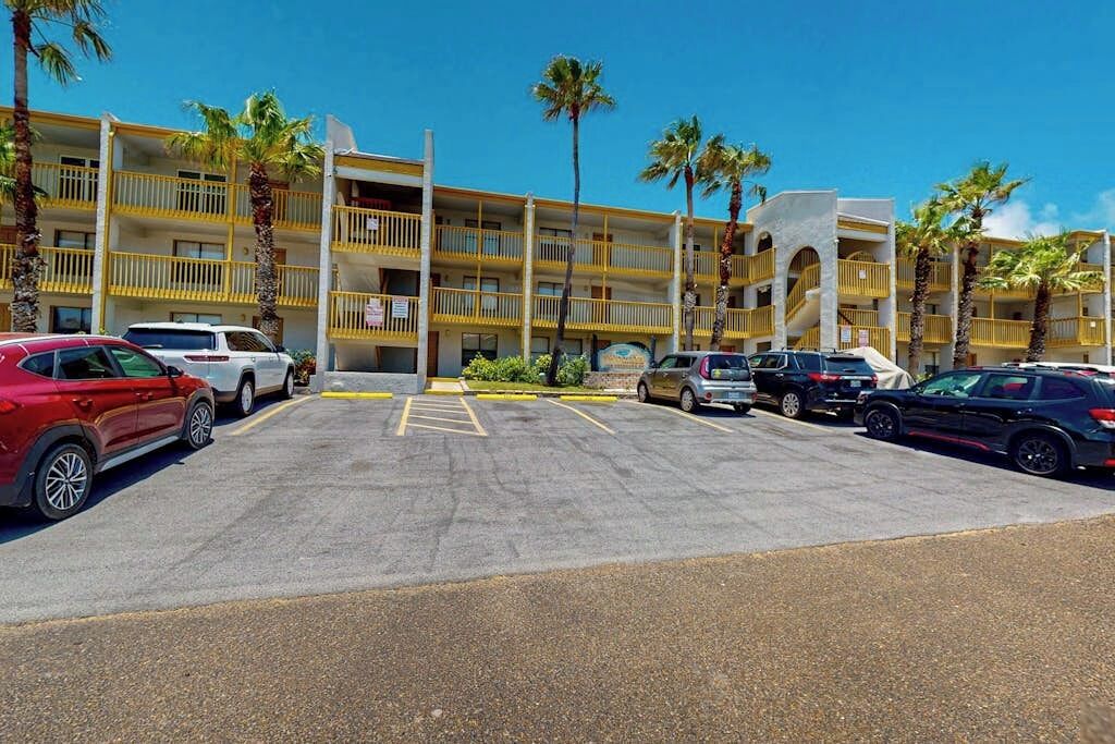 Un hôtel à plusieurs étages doté d’un parking, de palmiers et surplombant un ciel d’un bleu limpide.