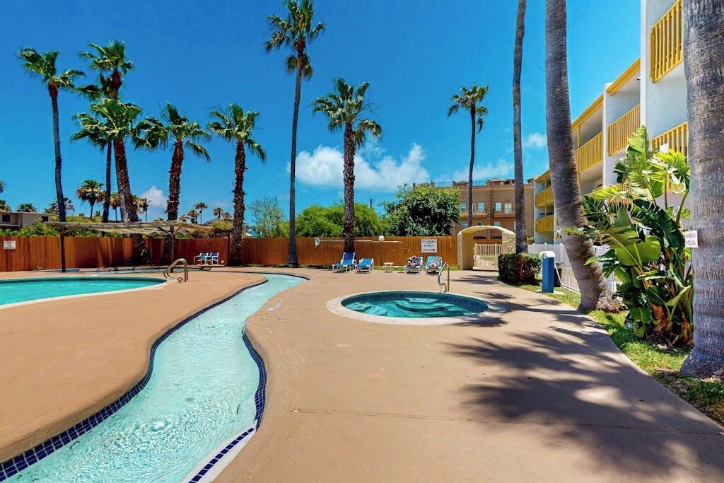A pool area with two swimming pools, palm trees, and a building with balconies.