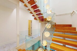 A modern interior with a glass staircase and wooden steps. - Shibui Home - Private Pool, Steps to Sand (South Padre Island)