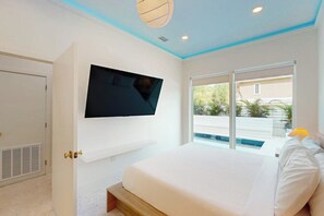 A bedroom with a bed, a TV mounted on the wall, and a window with a view of the outside. - Shibui Home - Private Pool, Steps to Sand (South Padre Island)