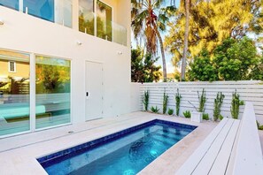 A modern outdoor swimming pool area with a glass door entrance, a wooden deck, and a white fence. - Shibui Home - Private Pool, Steps to Sand (South Padre Island)