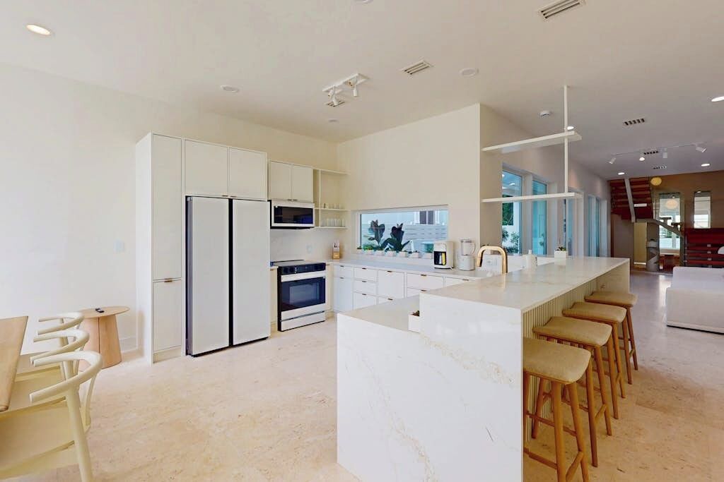 A modern kitchen with white cabinetry, a central island with bar stools, and a view to the outside.