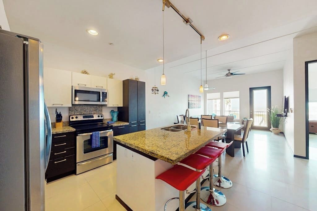 A modern kitchen with a central island, stainless steel appliances, and a dining area with red bar stools.