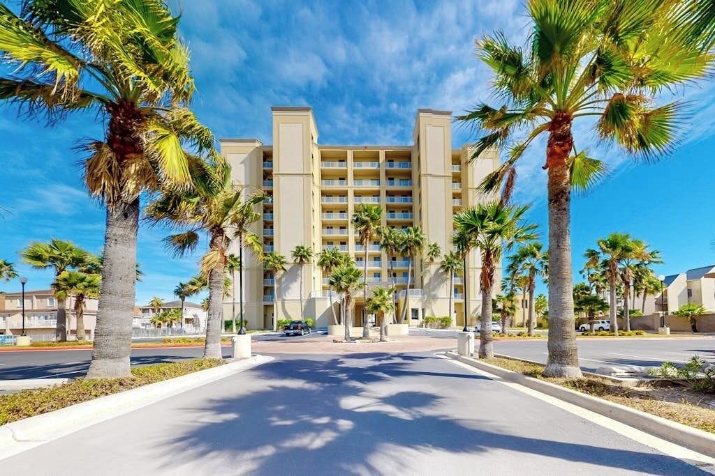 A hotel with a central courtyard, palm trees, and a clear blue sky.