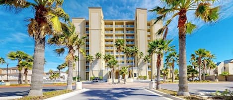 A hotel with a central courtyard, palm trees, and a clear blue sky.
