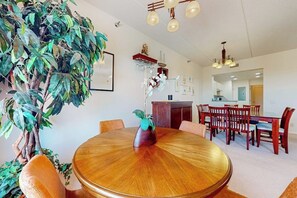 A round wooden dining table with chairs, a potted plant, and a hanging light fixture. - Palm Frond Sanctuary, Unit 302 (South Padre Island)