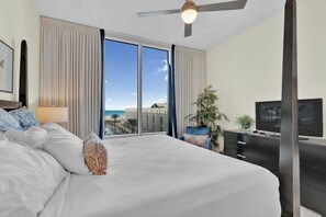 A hotel room with a large bed, a television, a desk, and a view of the ocean. - Sapphire Condominiums #408 (South Padre Island)