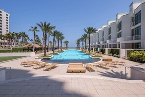 Piscina com espreguiçadeiras e palmeiras, cercada por edifícios modernos.