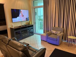 A living room with a television, a sofa, a chair, a small table, and a sliding glass door leading to an outdoor area. - Sapphire Condominiums #408 (South Padre Island)