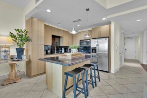A modern kitchen with a central island, stainless steel appliances, and bar stools. - Sapphire Condominiums #408 (South Padre Island)