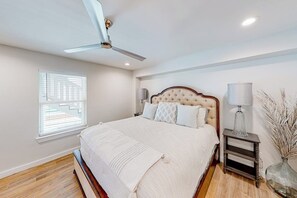 Ein Schlafzimmer mit einem Bett, einem Deckenventilator, einem Nachttisch mit Lampe und einem Fenster mit Jalousien.
