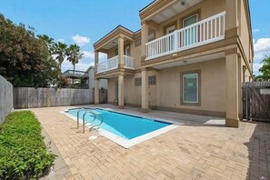 A two-story building with a swimming pool, a wooden fence, and a clear sky. - Island Breeze Retreat on Jupiter (South Padre Island)