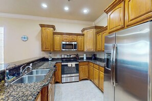 A kitchen with wooden cabinets, stainless steel appliances, granite countertops, and a clock on the wall. - Island Breeze Retreat on Jupiter (South Padre Island)