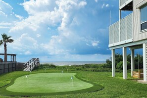 A golf course with a view of the ocean, a wooden deck, and a building with a balcony. - The Beach Escape - Beachfront Home, Sleeps 16 (Galveston)