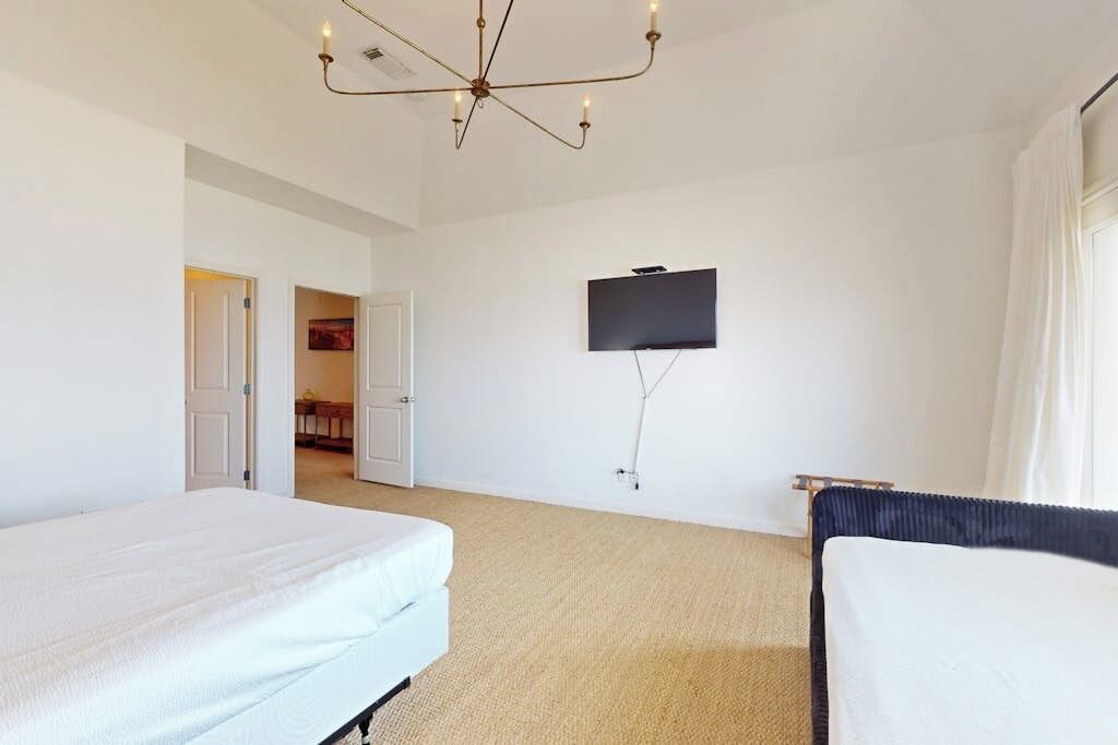 A hotel room with a bed, a television mounted on the wall, and a chandelier.