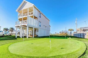 A two-story building with a balcony, a well-maintained lawn, and a golf course. - The Beach Escape - Beachfront Home, Sleeps 16 (Galveston)