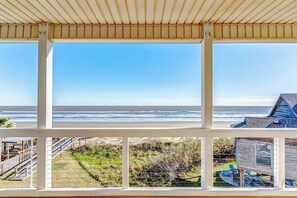 A coastal view from a covered balcony with a wooden railing, overlooking the ocean and a beach. - The Beach Escape - Beachfront Home, Sleeps 16 (Galveston)