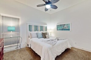 A bedroom with a bed, a ceiling fan, a window with blinds, a bedside table, and a wall-mounted lamp. - The Beach Escape - Beachfront Home, Sleeps 16 (Galveston)