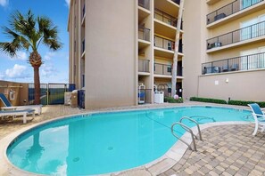 A swimming pool with a palm tree, lounge chairs, and a multi-story building with balconies. - Seagull Condominiums #301 (South Padre Island)