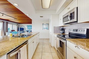A modern kitchen with a granite countertop, stainless steel appliances, and a wooden ceiling. - Seagull Condominiums #301 (South Padre Island)
