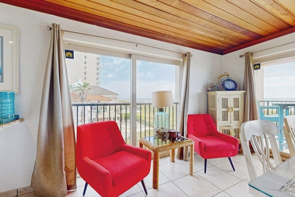 A balcony with two red chairs, a small table, and a clock.