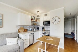 A compact kitchen with white cabinets, a wooden table, and a clock on the wall. - Wandless Waves - Pool & Hot Tub, Steps to Sand (Galveston)