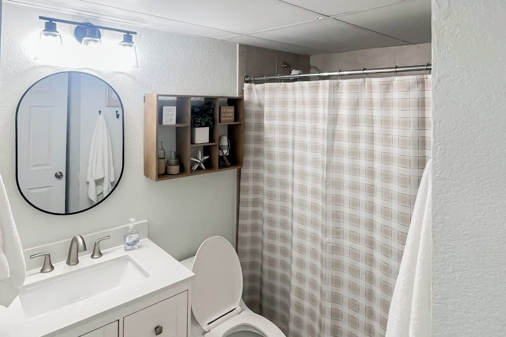 A bathroom with a white sink, a mirror, a toilet, and a shower curtain.