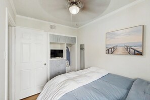 Ein Schlafzimmer mit Bett, Kleiderschrank, Fernseher und einem Gemälde an der Wand.