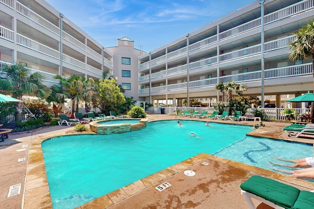 A hotel pool area with multiple levels of balconies, lounge chairs, and a central swimming pool.