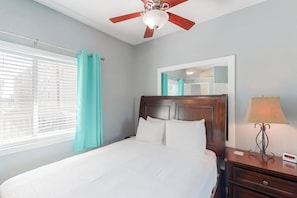 A hotel room with a bed, a nightstand, a lamp, a ceiling fan, a window with curtains, and a mirror. - Leeward Isles 305 - Pool, Near the Beach, Dogs OK (Corpus Christi)