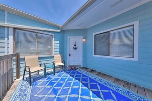 A covered porch with two chairs, a patterned rug, and a white door with an anchor decoration. - Leeward Isles 207 - Pool, Walk to the Water (Corpus Christi)