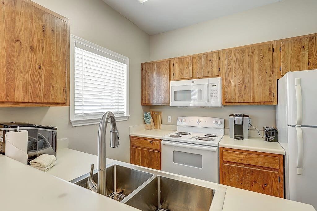 A compact kitchen with wooden cabinets, a microwave, a stove, and a sink.
