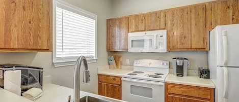 A compact kitchen with wooden cabinets, a microwave, a stove, and a sink.