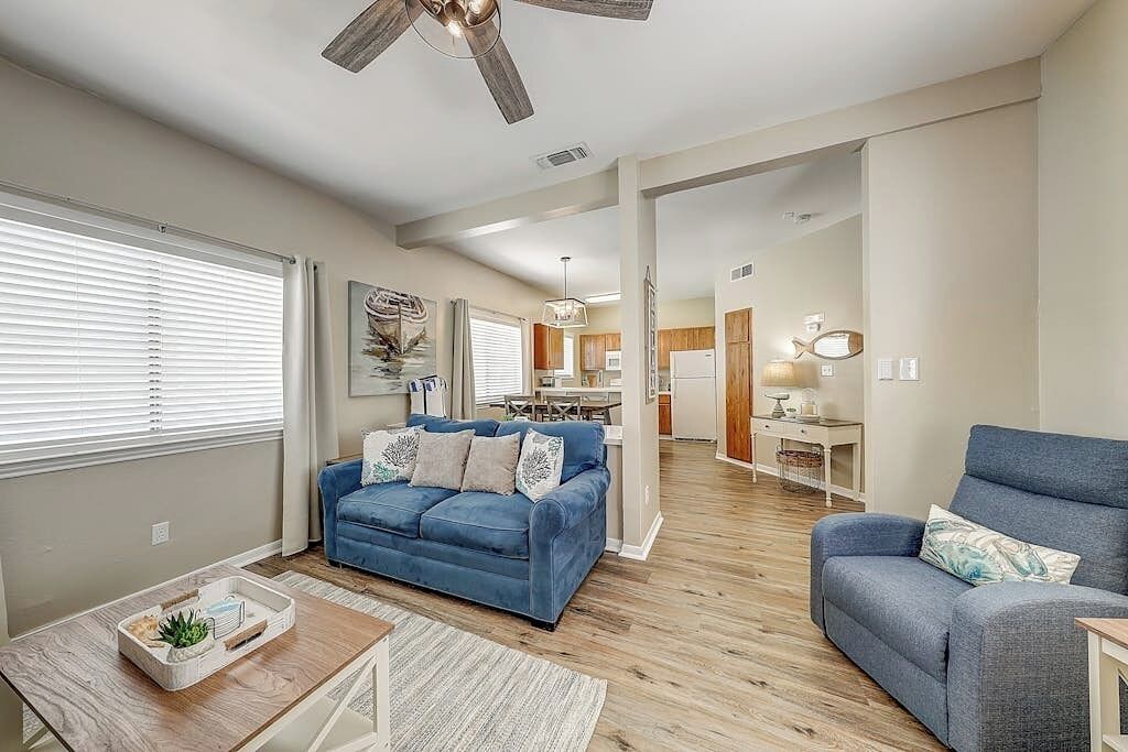 A spacious living room with a blue sofa, a coffee table, and a ceiling fan.
