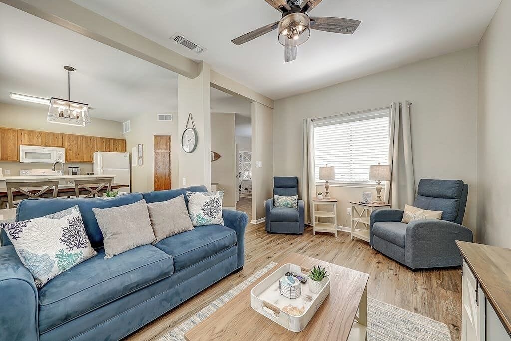 Un salon avec un canapé bleu, deux fauteuils, une table basse et un ventilateur de plafond.