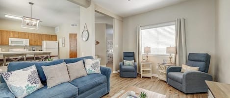 Un salon avec un canapé bleu, deux fauteuils, une table basse et un ventilateur de plafond.