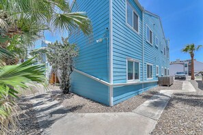 Ein zweistöckiges Haus mit blauer Fassade, einer Betonauffahrt und einem kleinen Garten mit Palmen.