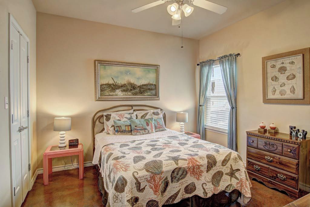 A bedroom with a bed, a nightstand, a dresser, a ceiling fan, and a window with curtains.