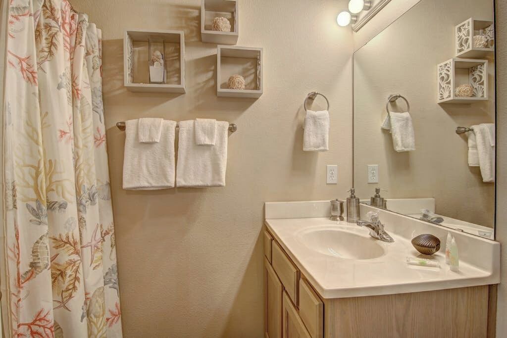 Un baño con lavamanos, espejo y toalleros.