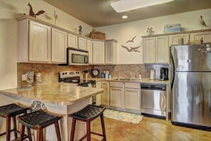 A kitchen with white cabinetry, a granite countertop, a stainless steel refrigerator, and a microwave. - Palm Bay 307 - Heated Pool, Walk to the Beach (Corpus Christi)