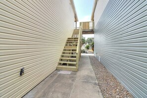 A narrow outdoor corridor with a wooden staircase leading to a higher level. - The Moor The Merrier (Port Aransas)