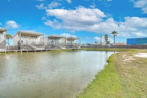 A waterfront property with a dock, a small building, and a grassy area. - The Moor The Merrier (Port Aransas)