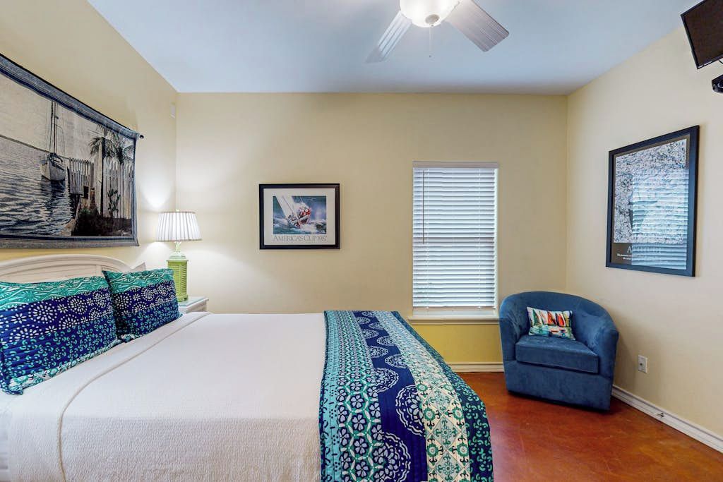 Une chambre à coucher avec un lit, une chaise, une fenêtre avec des stores et un ventilateur de plafond.