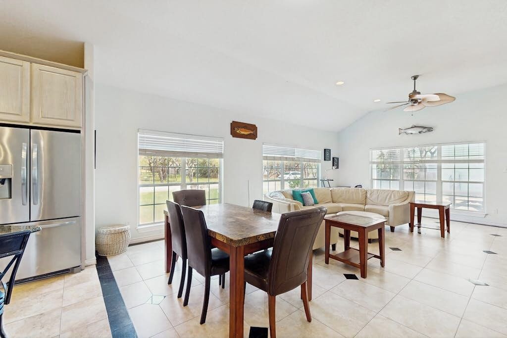 A spacious kitchen with a dining area, large windows, and a ceiling fan.