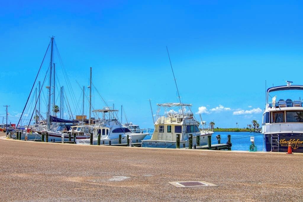 Un port esportiu amb diverses embarcacions amarrades, un cel blau clar i una massa d'aigua tranquil·la.