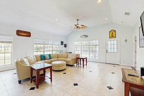 A spacious living room with a beige sectional sofa, a round ottoman, and a ceiling fan. - Fulton Bliss - Boat Parking, Porch & Dogs OK (Rockport)