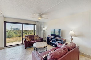 A living room with a sofa, a coffee table, a TV, and a ceiling fan. - Island House #105 - Heated Pool & Outdoor Patio (Corpus Christi)