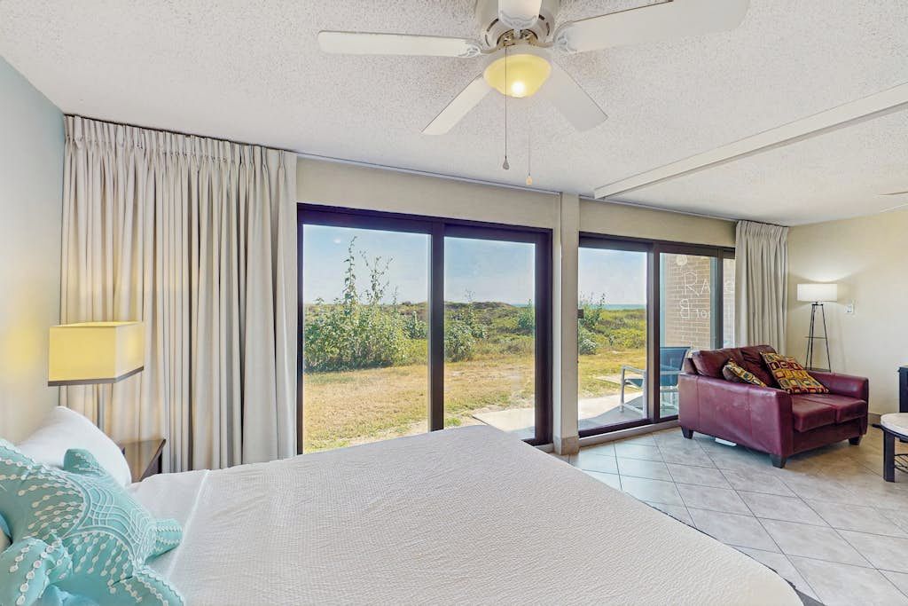 Habitación de hotel con cama, sofá rojo, lámpara de pie y vistas a través de amplias puertas de cristal.