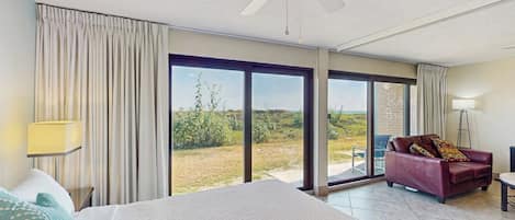 Habitación de hotel con cama, sofá rojo, lámpara de pie y vistas a través de amplias puertas de cristal.